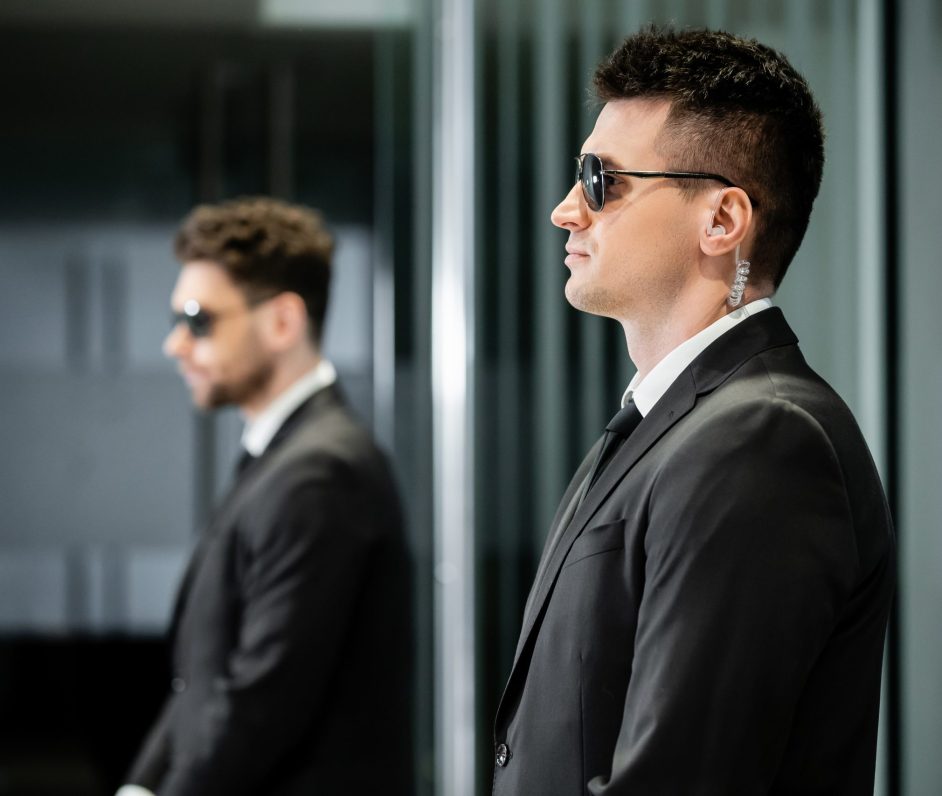 bodyguard service, private security, professional in suit and sunglasses standing in hotel lobby near work partner, earpiece, communication, luxury hotel, vigilance, protection and work, side view